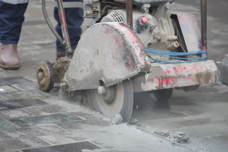 Betonsägearbeiten: Eine Betonsäge schneidet den Straßenbelag, Staub und Schutt liegen in der Luft.
