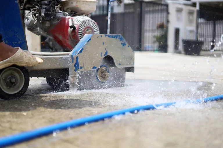 Betonsägearbeiten auf nassem Straßenbelag, Wasser- und Staubspritzer von der Säge.