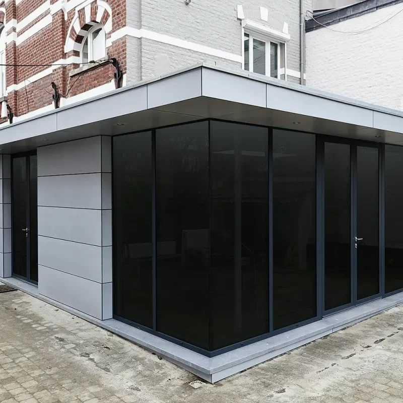 Moderne Anbauten aus Glas und Metall, die an die Fassade eines klassischen Backsteinhauses angebaut sind.