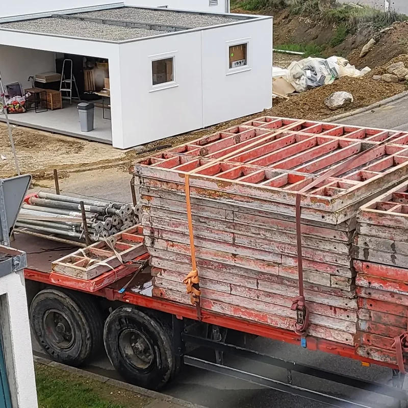Ein großer Lkw, beladen mit Materialien für Betonarbeiten, steht in der Nähe eines weißen Gebäudes.