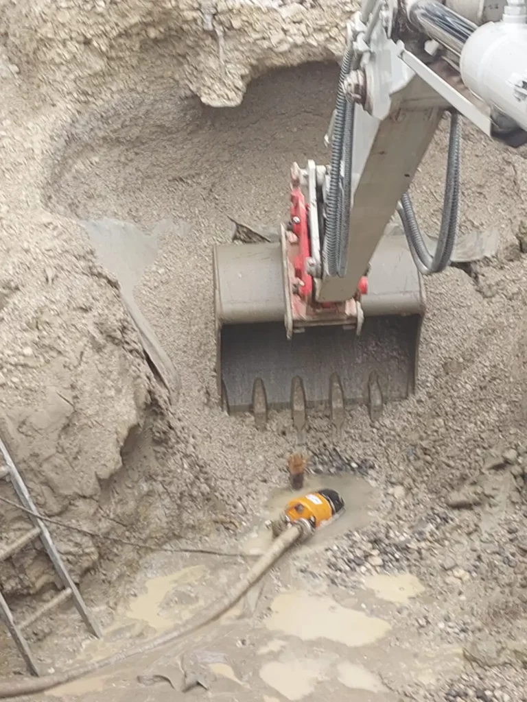Bagger bei Erdarbeiten und Entwässerungsarbeiten in schlammigem Wasser auf felsigem Untergrund.
