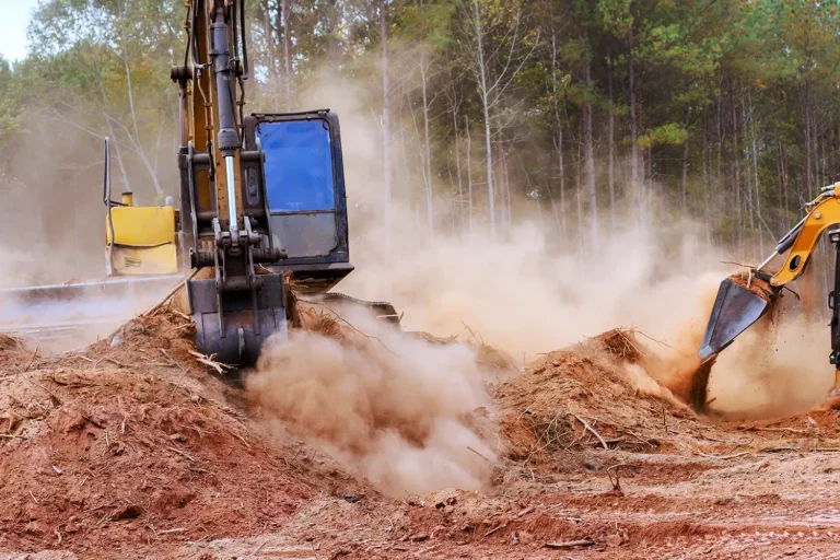 Bagger für den Straßenbau und die Landwirtschaft auf einer staubigen Baustelle in der Nähe von Bäumen.
