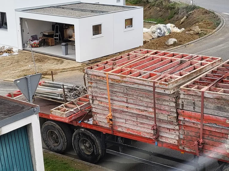 Ein großer Lkw, beladen mit Materialien für Betonarbeiten, steht in der Nähe eines weißen Gebäudes.